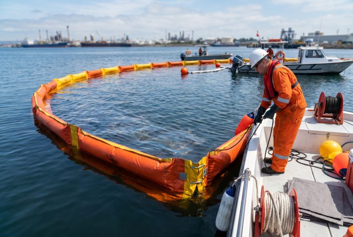 Worker deploying oil spill cleanup boom on calm waters